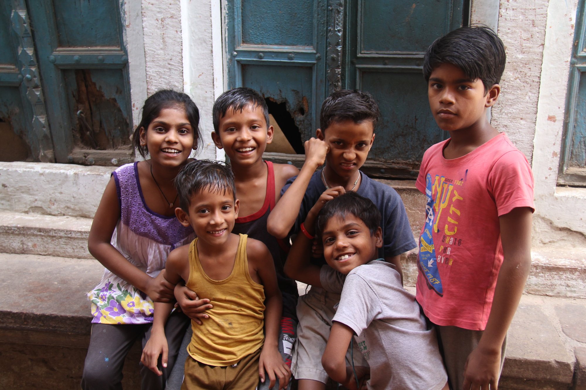 A group of children grinning in front of a blue door in India
